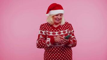 senior grootmoeder gebruik makend van mobiel telefoon typen nieuw post Aan web, Kerstmis boodschappen doen online, browsen video