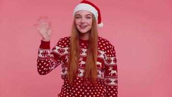 Woman in Christmas sweater waves hand palm in hello gesture welcomes someone to celebrate New Year video