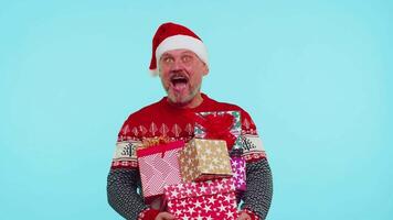 Man in Christmas red sweater, Santa hat, smiling, holding many gift boxes New Year presents shopping video