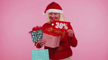 Senior woman in Christmas sweater showing gift box and 30 Percent discount inscriptions banner text video