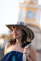 hermosa mujer vistiendo el tradicional Colombiana sombrero llamado sombrero vueltiao a el reloj torre en el histórico calles de el cartagena Delaware indios amurallado ciudad foto