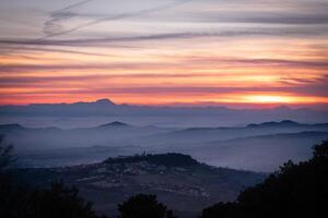 Sunset landscape on the mountains fire in the sky with clouds and dramatic vibes sun going down while fog hugs all the valleys photo