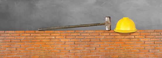 Helmet and hammer on red brick wall. Cement background. photo