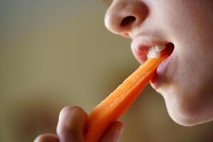 Crop anonymous teenage girl eating fresh organic carrot slice photo