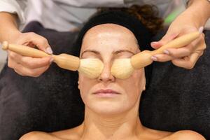 Crop beautician applying cosmetic product with brushes in beauty salon photo