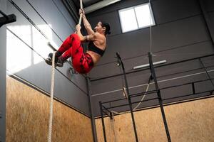 Fit mature woman climbing a rope in a gym photo