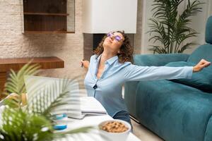 Happy woman stretching arms near laptop at home photo