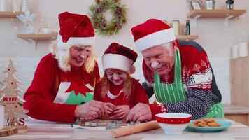 Senior family grandparents with granddaughter in Santa Claus hats preparing, cooking homemade cookie video