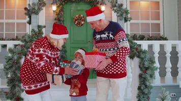 Senior grandparents with grandchild girl kid exhcanging gifts near Christmas house celebrating Xmas video