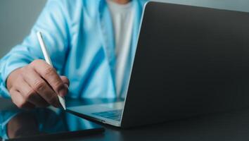 Businessman in black suit working on laptop computer and tablet, Hand touch on tablet at office with dark background, Online working, Close up, Copy space. photo