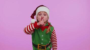 Child girl in Christmas Elf costume presses index finger to lips makes silence gesture sign, secret video