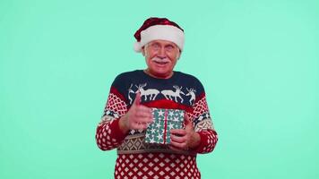 Grandfather in Santa sweater presenting one Christmas gift box, stretches out his hands to camera video