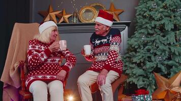 Senior old wife and husband talking, drinking tea near glowing xmas tree on Christmas in home room video