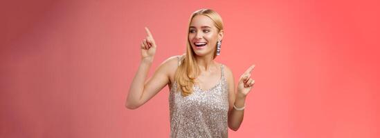 Carefree elegant joyful charming blond girlfriend dancing boyfriend party nightclub standing red background in silver glittering dress raising hands up moving body music rhythm, smiling photo