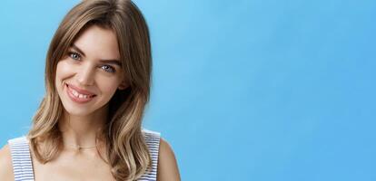 Waist-up shot of charming self-assured authentic woman feeling great accepting own imperfections tilting head smiling broadly at camera and showing cute gapped teeth posing over blue background photo