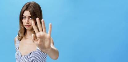 Silly and shy insecure attractive girl pulling hand towards to cover face from camera making moody timid expression asking to stop not liking what happening saying no with body language over blue wall photo