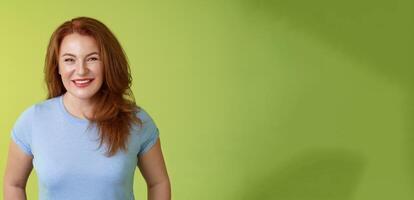 Cheerful kind happy redhead middle-aged mother look caring delighted smiling broadly gaze admiration joy stand blue t-shirt green background amused enthusiastic expression photo