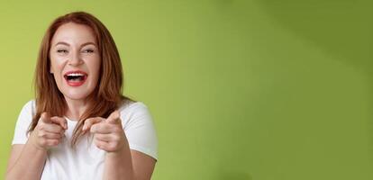 You did best. Friendly joyful enthusiastic redhead ginger middle-aged female pointing index fingers camera finger pistol gesture smiling broadly congratulate cheer coworker stand green background photo