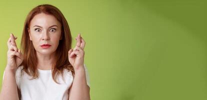 Stunned intense worried middle-aged redhead woman stare nervously awaiting important result implore dream come true receive positive reply standing stupor green background make wish good luck photo