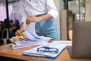 secretary is searching through pile of important documents on office table deliver them to manager for presentation in time at meeting. Concept of difficulty finding information from piles of document photo