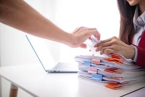 A young secretary receives a pile of documents to find important information for the company manager to use in a meeting. The concept of finding important documents from piles of overlapping documents photo