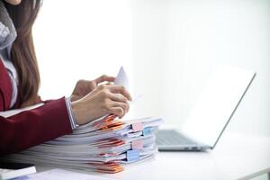 secretary is searching through pile of important documents on office table deliver them to manager for presentation in time at meeting. Concept of difficulty finding information from piles of document photo