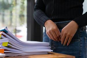 secretary is searching through pile of important documents on office table deliver them to manager for presentation in time at meeting. Concept of difficulty finding information from piles of document photo