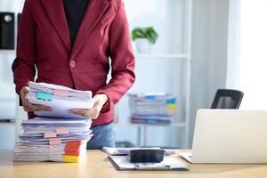secretary is searching through pile of important documents on office table deliver them to manager for presentation in time at meeting. Concept of difficulty finding information from piles of document photo