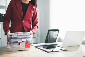 secretary is searching through pile of important documents on office table deliver them to manager for presentation in time at meeting. Concept of difficulty finding information from piles of document photo