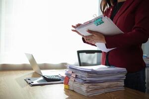 secretary is searching through pile of important documents on office table deliver them to manager for presentation in time at meeting. Concept of difficulty finding information from piles of document photo