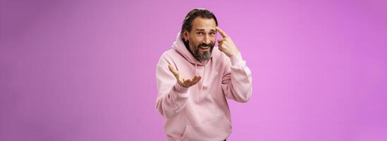 Outraged pissed man angry person crazy out of mind yelling bothered furiously gesturing rolling index finger temple accusing someone insane stupid, standing displeased intense purple background photo