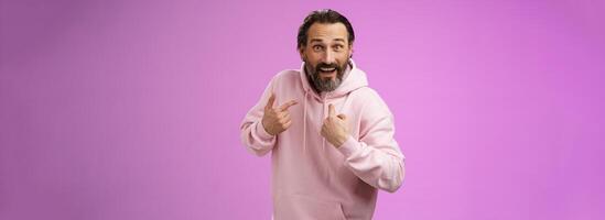 Excited surpried caucasian bearded guy pointing himself amazed questioned cannot believe was picked chosen standing thrilled purple background become winner lottery wearing pink hoodie photo