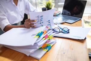 secretary is searching through pile of important documents on office table deliver them to manager for presentation in time at meeting. Concept of difficulty finding information from piles of document photo