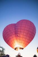 heart shaped hot air balloon floats over field of flowers in evening, and heart shaped balloons are also symbol of love and friendship. using heart shaped balloons as symbol of love and friendship. photo