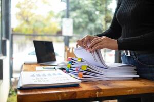 secretary is searching through pile of important documents on office table deliver them to manager for presentation in time at meeting. Concept of difficulty finding information from piles of document photo
