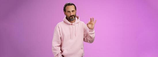 Confident good-looking lucky old macho guy bearded grey hair in stylish pink hoodie hold hand pocket show okay ok approval gesture smirking delighted agree daughter choice, posing supportive photo