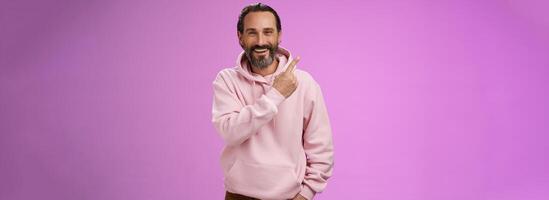 Charming friendly happy mature man 50s bearded grey hair laughing happily pointing upper left corner behind showing proudly family members standing purple background having fun stay positive photo