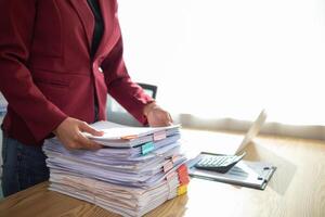 secretary is searching through pile of important documents on office table deliver them to manager for presentation in time at meeting. Concept of difficulty finding information from piles of document photo
