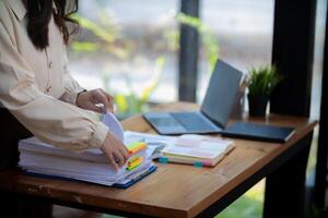 secretary is searching through pile of important documents on office table deliver them to manager for presentation in time at meeting. Concept of difficulty finding information from piles of document photo
