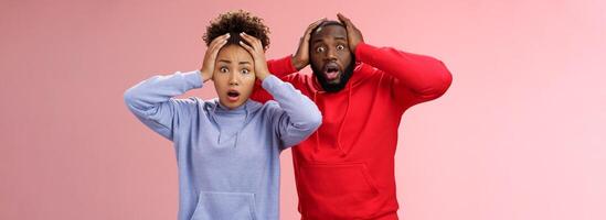 Shocked worried african american couple man woman holding hands head panicking widen eyes stunned receive bad concerning news feel troubled nervous, standing pink background anxious photo