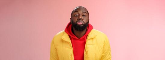 Portrait bored childish cute african bearded 25s male show tongue grimacing making funny faces immature behaviour unwilling grow-up standing pink background mimicking folding lips tube photo