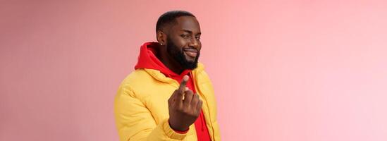 Cheeky flirty black bearded guy asking come closer beckon index finger camera smiling make smug face have plans for you alluring join, standing pink background devious grin photo