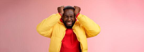 Depressed heartbroken black bearded boyfriend go crazy pissed squeez head frowning squinting clenching teeth painful feeling inside standing devastated distressed pink background suffering headache photo