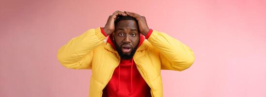 Shocked stupefied young african-american bearded man grab head drop jaw gasping confused frustrated looking upset troubled have problems standing stunned concerned pink background photo