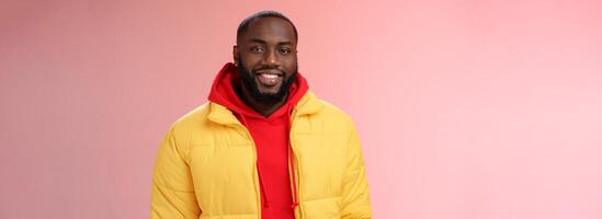 Waist-up happy charismatic good-looking bearded guy in yellow jacket red hoodie smiling joyfully white perfect smile talking have nice friendly conversation, standing pink background photo