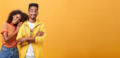 Guy feeling happy girl lean on his shoulder grinning and chuckling from happiness standing pleased and joyful over orange background while woman hugging best friend upbeat she can rely on him photo