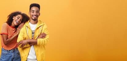 Awesome when boyfriend is best friend. Portrait of charming friendly african american woman leaning on guy touching his shoulder feeling happy they together and she can rely on posing orange wall photo