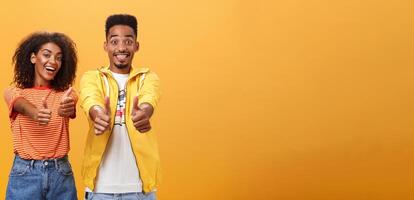 Two friends like perfect and awesome plan. Portrait of joyful friendly-looking optimistic african american female and male showing thumbs up in approval and agreement gesture smiling broadly photo