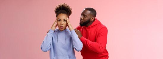 Man apologizing girlfriend behind back touching shoulder comforting girl feel pressured irritated fed up lying hear boyfriend sorry arguing standing bothered pink background, couple fighting photo