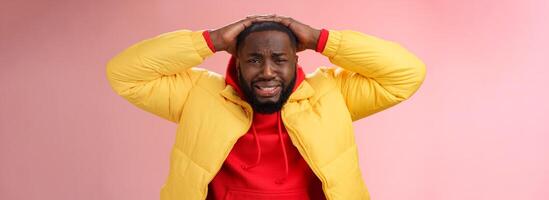 Upset unhappy african-american male entrepreneur lose money feel regret sadness grimacing painful heartbreaking feelings, holding hands head depressed devastated, standing pink background photo